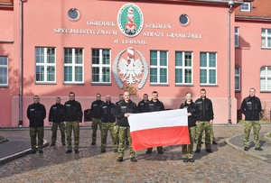 Grupa funkcjonariuszy SG z flagą na tle budynku