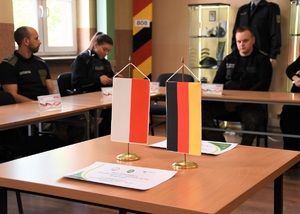 Na stole stoją dwie flagietki : polska oraz niemiecka. W tle siedzą uczestnicy szkolenia