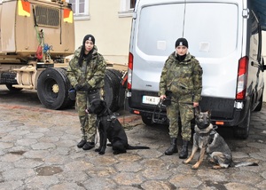 Dwie funkcjonariuszki SG z psami służbowymi w tle pojazd służbowy