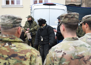 Na pierwszym planie trzech amerykańskich żołnierzy, w tle funkcjonariusze SG oraz kobieta ubrana w kostium do pełnego gryzienia