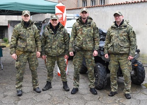 Czterech funkcjonariuszy SG w tle pojazd służbowy SG oraz słup graniczny