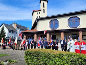 Poczty sztandarowe służb mundurowych oraz szkół biorące udział w uroczystości na tle kościoła.