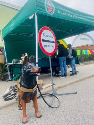 Stoisko promocyjne OSS SG na pierwszym planie manekin przypominający psa w tle znak kontrola graniczna oraz uczestnicy pikniku