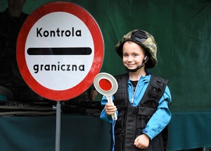 Chłopiec ze sprzętem służbowy SG. W tle znak kontrola graniczna