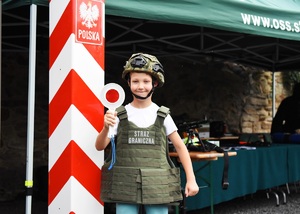 Chłopiec ze sprzętem służbowym SG. W tle Stoisko promocyjne