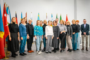 Zdjęcie grupowe uczestników i wykładowcy kursu na tle flag