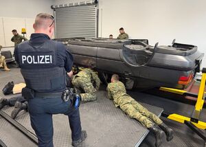 Na pierwszym planie stojący funkcjonariusz Policji, w tle obrotnica i funkcjonariusze SG