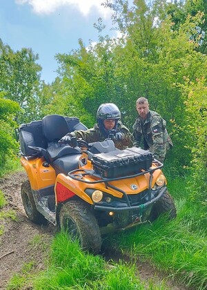 Szkolimy się na ATV Funkcjonariuszka SG na pomarańczowym pojeździe ATV podczas zajęć w terenie. Obok niej Funkcjonariusz SG prowadzący zajęcia