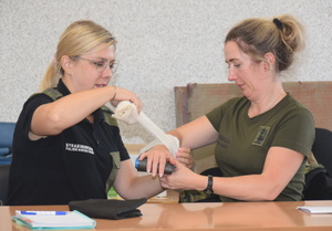 Zakończenie kursu z zakresu udzielania pierwszej pomocy W sali wykładowej funkcjonariuszka SG opatruje ranę na przedramieniu drugiemu funkcjonariuszowi SG